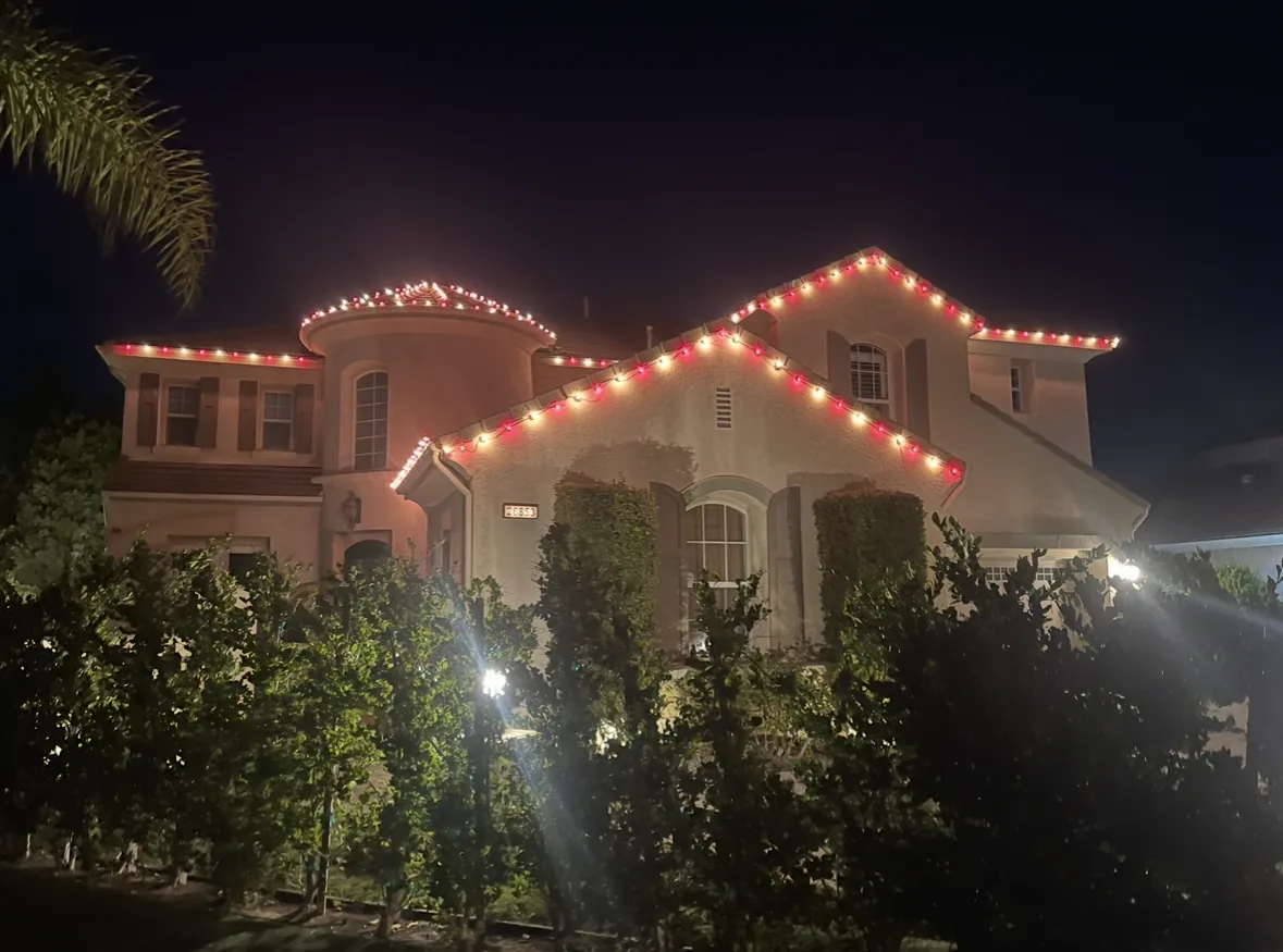 Professional holiday lighting: two-story stucco home with red and warm white C9 roofline lights
